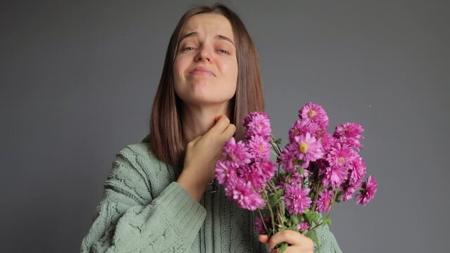 Pollen season. Rhinitis reaction. Chrysanthemum allergy. Seasonal disease. Sick woman wearing green knitted shirt holding bouquet in hands, isolated over gray background suffering neck itch