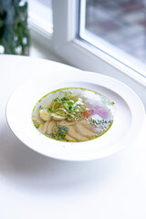 soup with meat and herbs in a white plate on the windowsill