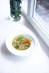 soup with meat and herbs in a white plate on the windowsill