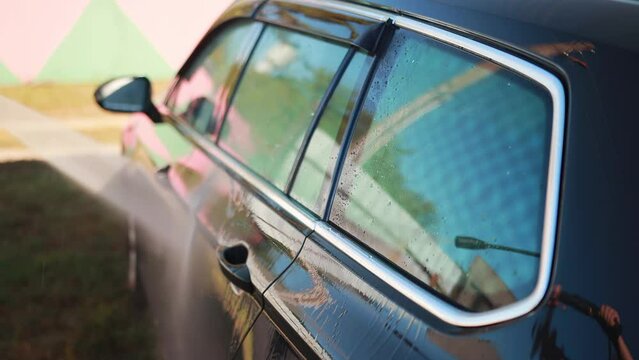 Washing a gray car outdoors in summer with a mini high-pressure washer. A jet of water under pressure washes away dirt on a car. Slow motion
