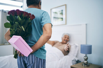 Gift, surprise and a senior couple on their anniversary in the bedroom of their house together for celebration in the morning. Flowers, birthday box and an old man giving his wife a present at home