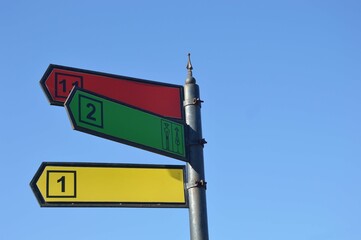 A pillar with colored direction arrows and destination numbers against the sky. Metal street sign. Place for names.