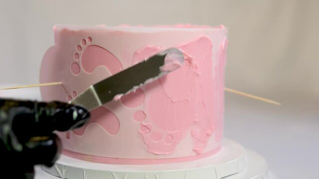 preparing birthday cake for birth of child decoration spreading pink cream on stencil in form of legs feet of child decoration professional pastry shop Christina birthday 1 year old baby. black gloves