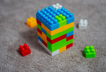 Big toy plastic blocks set as a town on beige brown carpet at children's room and chaos in background during playtime