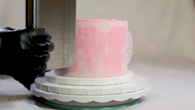 preparing birthday cake for birth of child decoration spreading pink cream on stencil in form of legs feet of child decoration professional pastry shop Christina birthday 1 year old baby. black gloves