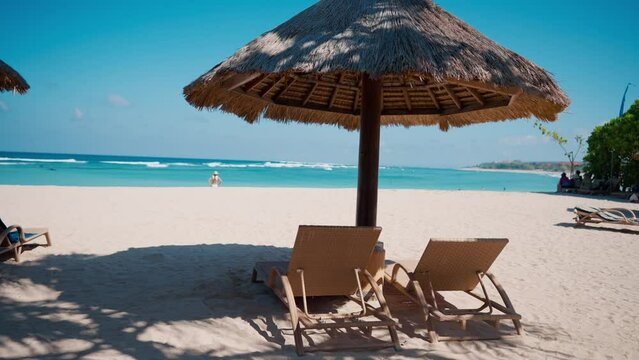 Wooden sunbeds on sandy beach under umbrella on tropical luxury resort in sunny summer day. Azure ocean water, waves and white sand. Amazing nature place for resting. Two lounge chairs on seashore.