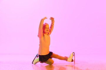 Beautiful, cute little girl, child, training figure skating against pink background in neon light....