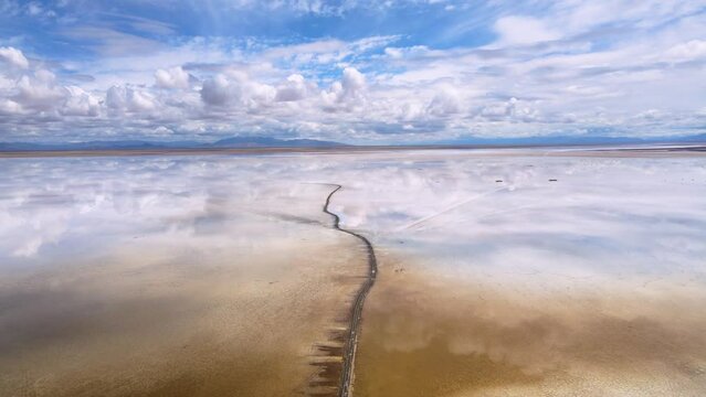 Drone shot flying over the Salinas Grandes salt lake on the border of Salta and Jujuy, Argentina following a dirt path.