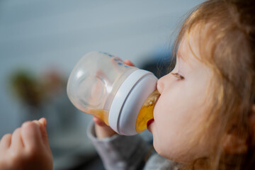 Baby toddler girl drinking tea from baby bottle close up with long hair