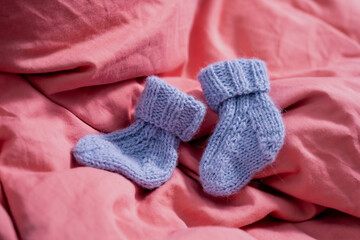 Little small blue knitted wool socks on a background of pink blanket. Symbol to young infant not yet born children, also gender reveal party idea