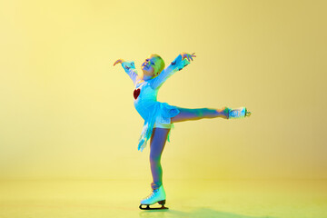 Full-length of cute, beautiful adorable kid, little girl, dancing, performing figure skating against yellow background in neon. Concept of childhood, figure skating sport, hobby, school, education