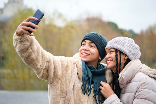 Happy dominican lesbian couple taking a selfie with the smartphone at street in winter.