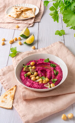 Beetroot hummus decorated with chickpeas on pink towel, pita bread, parsley on the white wooden table background