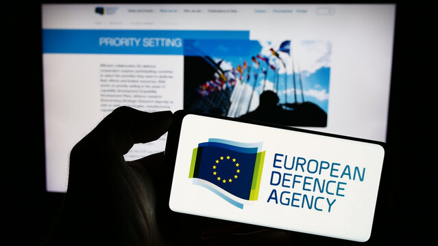 Stuttgart, Germany - 10-17-2023: Person holding cellphone with logo of EU institution European Defence Agency (EDA) in front of webpage. Focus on phone display.