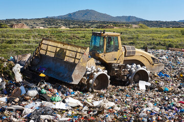 Fototapeta premium Heavy machinery shredding garbage in an open air landfill. Pollution