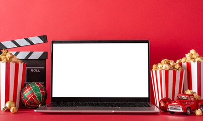 Winter staycation: side view of laptop, popcorn, baubles, movie clapper, and a tiny delivery car on...