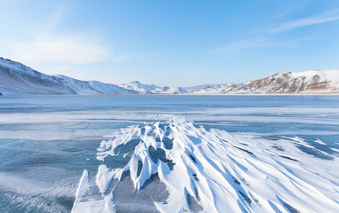 Winter landscape of frozen Baikal Lake in February cold sunny day. Сoastal mountains are covered...