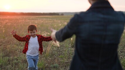 Boy runs along sunlit field with arms outstretched eager to embrace mother
