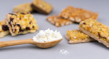 Whey protein powder in spoon and different energy protein bars on grey background. Close-up. Selective focus.