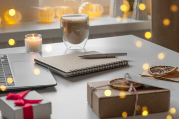 Obraz na płótnie Canvas Notepad with a pen, laptop, coffee cup, wrapped gifts on a desk table. Winter Festive atmospheric mood. Preparation for Christmas. Business Holidays Concept. Freelancer's desktop during Xmas vacation