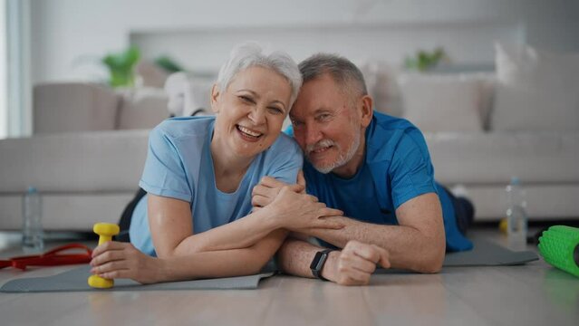 Portrait smiling old senior couple family lying on mat after home training looking at camera. Happy man woman together in living room. Sport active lifestyle fitness retired people pensioners concept.