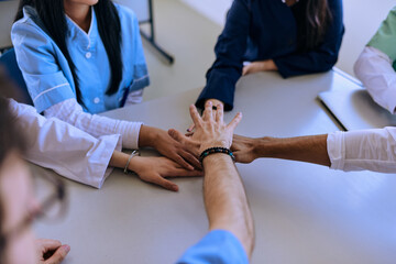 A group of doctors and a medical nurse join their hands together on a table, showcasing the...