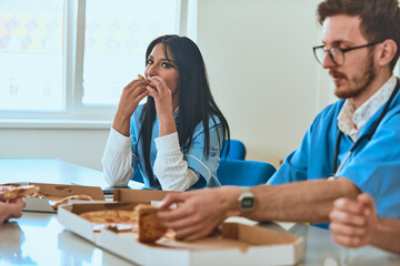 A group of doctors takes a well-deserved break in the hospital, savoring slices of pizza and...