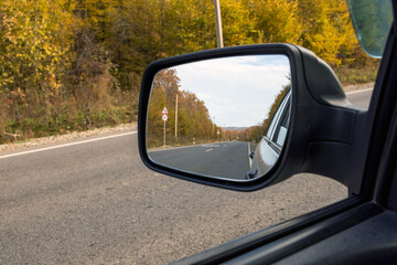 Car mirror, autumn road is reflected in the rear mirror of the car