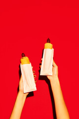 Two hands holding hot delicious traditional American hotdog with beef sausage and sauces against vivid red background. Concept of fast food, delivery.