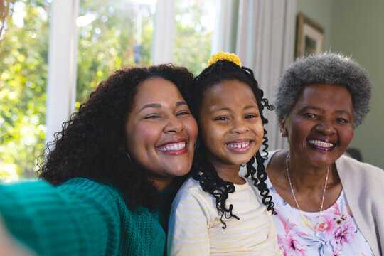 Happy african american mother, daughter and granddaughter embracing on couch at home, copy space