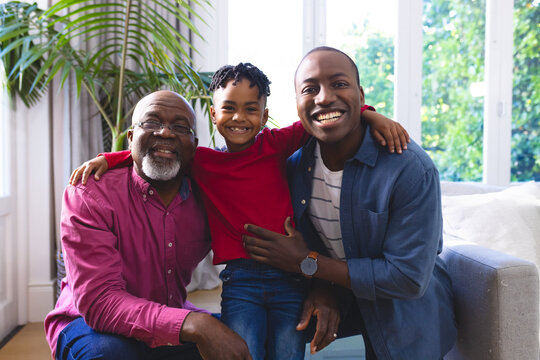Portrait of happy african american father, son and grandson embracing on couch at home, copy space