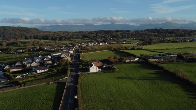 Aerial view circling over small town Welsh community farmland with Snowdonia mountain range on the horizon
