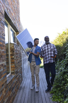 African american father with adult son carrying solar panel in garden, copy space