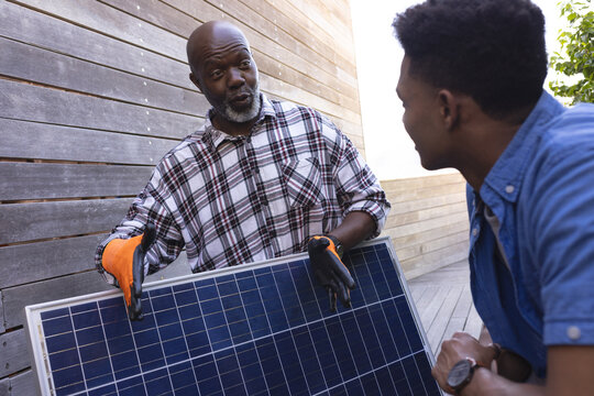 African american father with solar panel explaining to adult son in sunny garden - Powered by Adobe