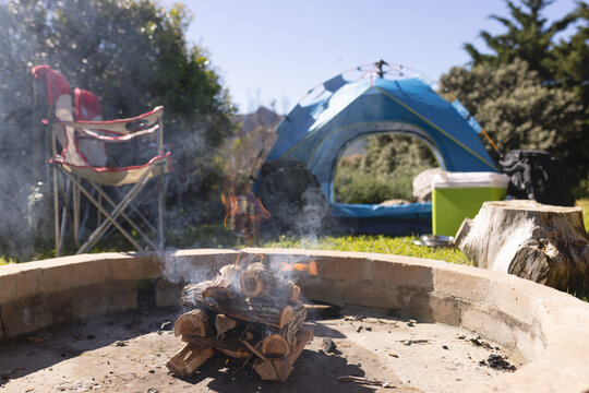 Firepit, tent, chairs and camping equipment at sunny rural campsite, copy space