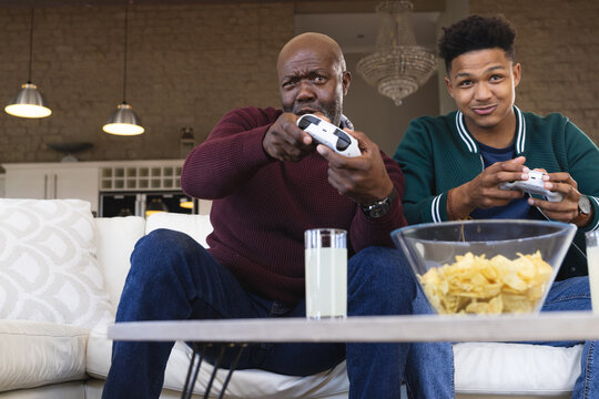 Focused african american father and adult son at home playing video game with gamepads