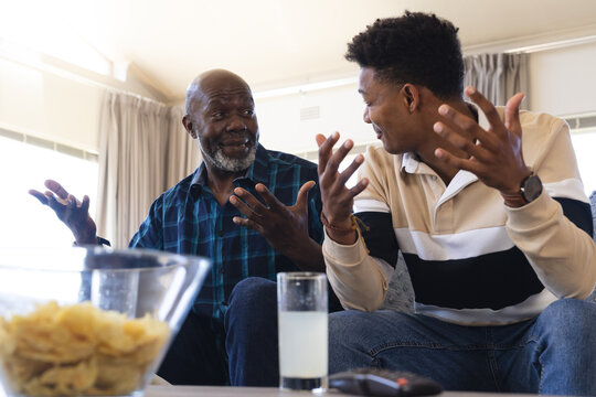 Surprised african american father and adult son watching sport on tv and gesturing to each other