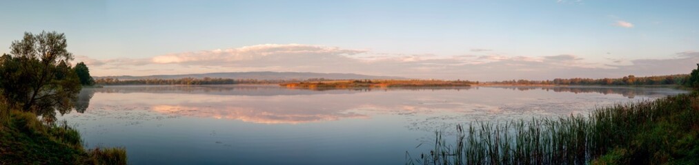 Panorama of the evening lake with a swan and the sun, colorful shades in the sky.