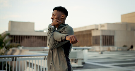 Black man, fitness and stretching on rooftop in city for workout, training or outdoor exercise. Happy African male person, runner or athlete in body warm up or arm stretch getting ready in urban town - obrazy, fototapety, plakaty