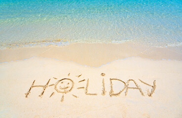 Holiday hand written in the sand on the beach blue waves in the background. Sun drawing on golden sand beach, holiday background sign concept.