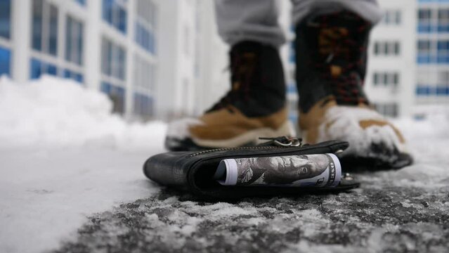 A lost wallet on the snowing path with hundred dollar bills in it close-up and a random man picks it up