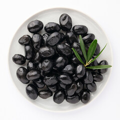 Delicious black olives in plate with olive tree sprig decoration isolated on white background top view for your design. Healthy eating, healthy fats for humans. Organic vegetable