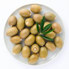 Delicious green olives almond inside in plate with olive tree sprig decoration isolated on white...