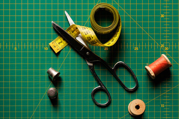 Tailor's meter, scissors and thimble close-up on the background of the cutting mat. View from above. - obrazy, fototapety, plakaty