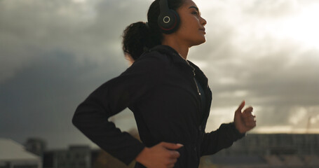 Fitness, music and a woman running in the city for health or cardio preparation of a marathon. Exercise, wellness or sports training and a young runner or athlete listening to audio with headphones - obrazy, fototapety, plakaty