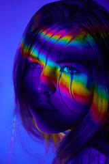 LGBTQIA. Close-up of young beautiful girl against blue background with multicolored neon lights on...