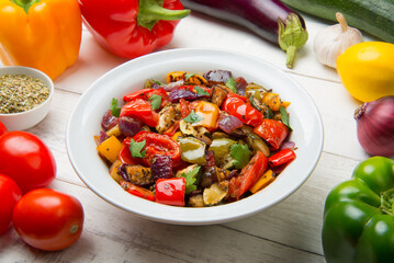 Mediterranean roasted vegetables in a salad bowl on a white rustic table with ingredients. - 671476590