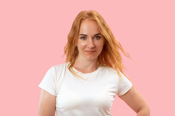 Portrait of young charming redhead woman with long wavy hair in white t shirt, pink background. Beautiful confident woman