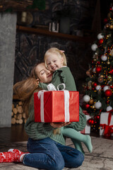 Portrait of happy mother and little daughter near Christmas tree with large Xmas presents. Vertical frame.
