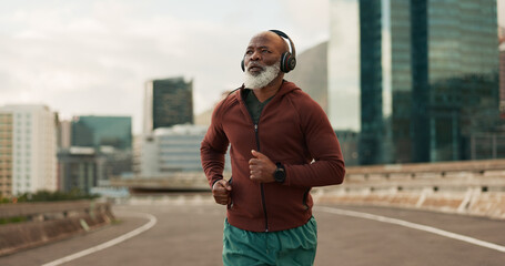 Running, city and senior man with headphones in training, streaming music and fitness. Retirement, black person or wellness of african runner for race in progress, urban road or marathon competition - obrazy, fototapety, plakaty